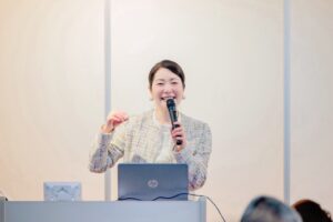 西川株式会社様にて開催した笑顔ワークショップの様子。笑顔専門家 川野恵子が、笑顔・コミュニケーション・接客力向上について講演している場面。
